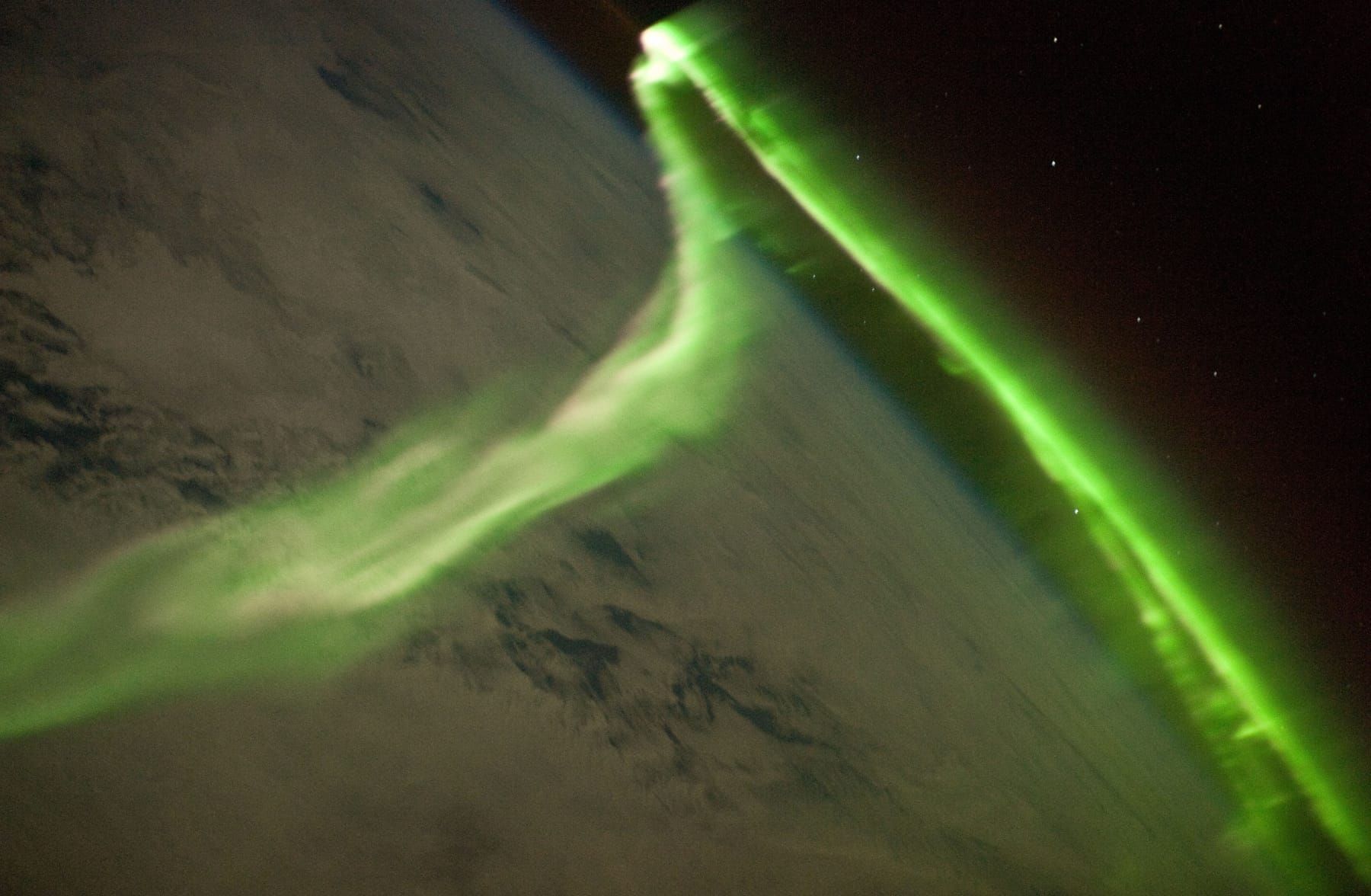 Bright green curtains of the southern lights over clouds, photographed from orbit