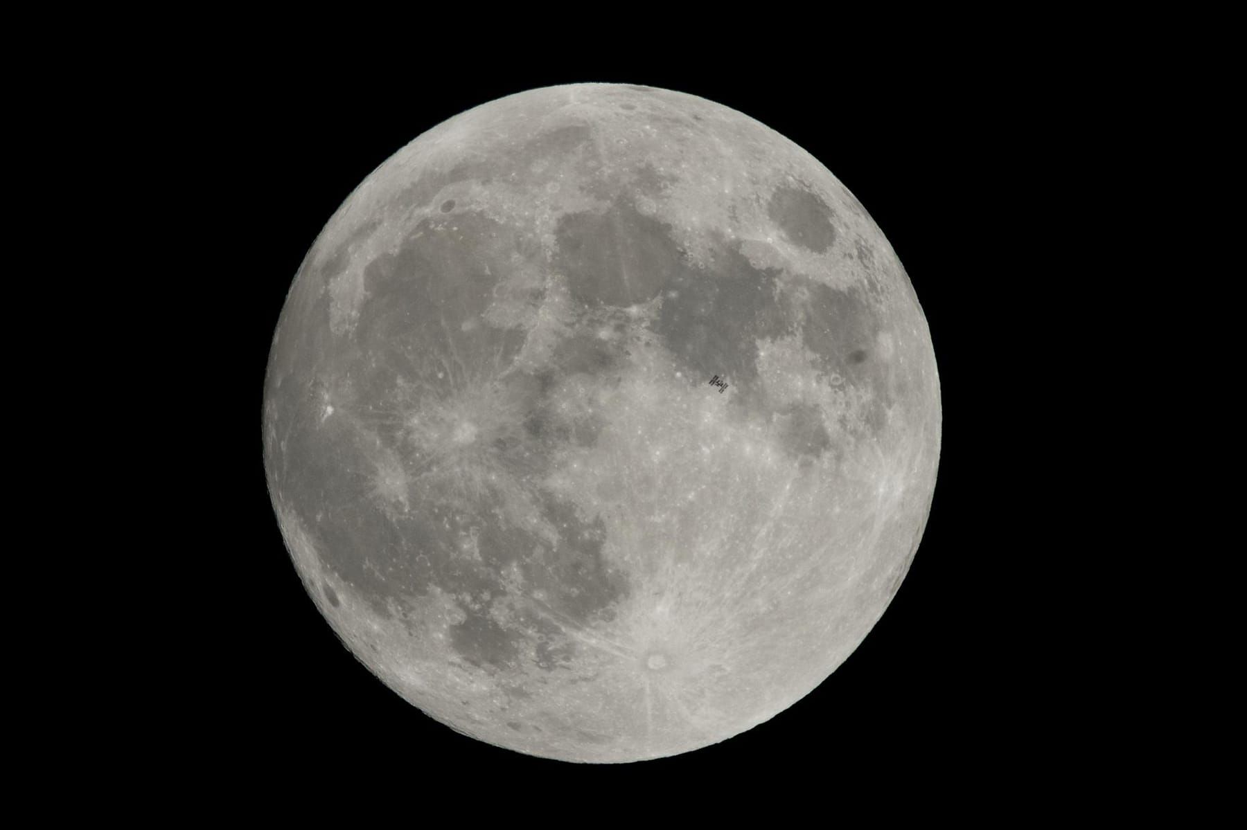 The tiny silhouette of the International Space Station in front of the full Moon