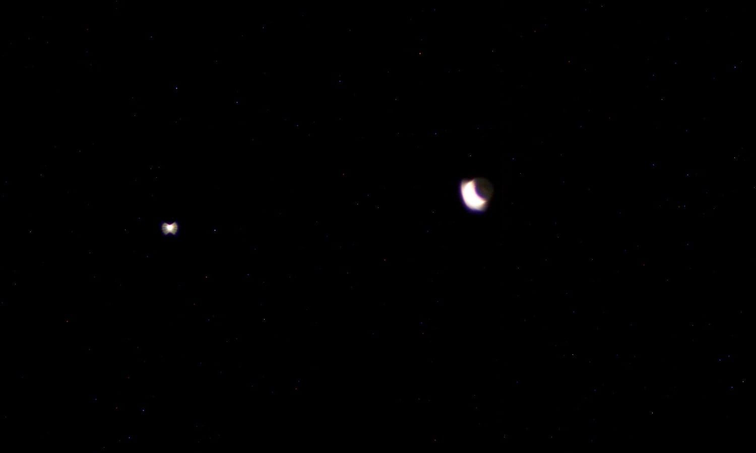 A thin crescent Moon with its dark side faintly lit by earthshine, next to the bright point of Venus